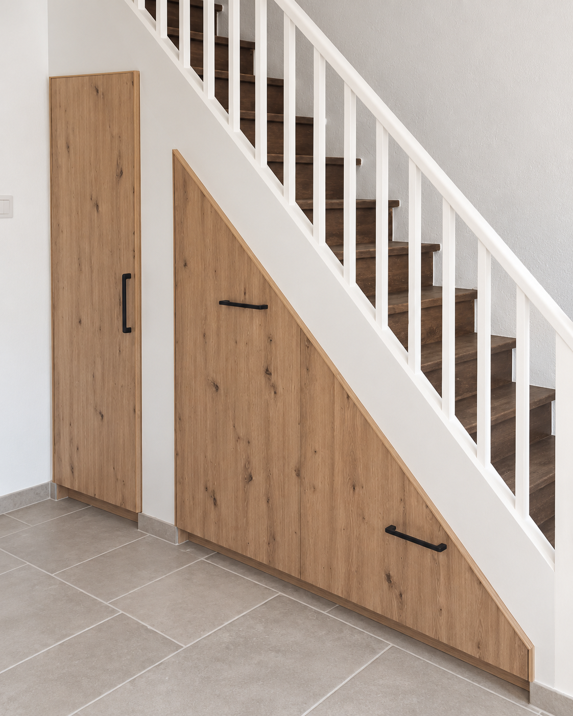 Aménagement sous escalier sur mesure coloris bois avec portes qui suivent la géométrie de l’escalier.