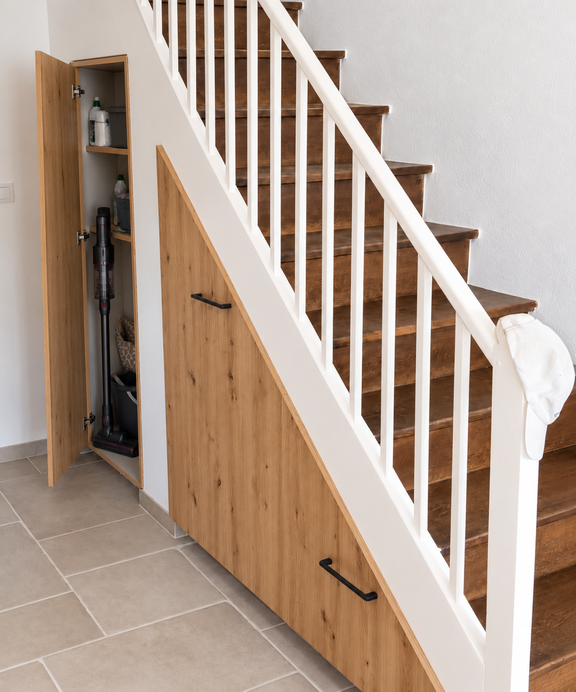Aménagement sous escalier sur mesure coloris bois avec portes qui suivent la géométrie de l’escalier.