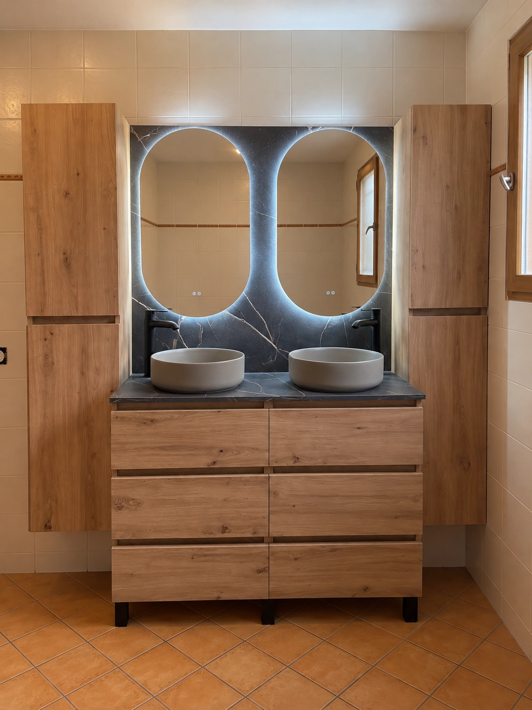 Vue de face d'un aménagement de salle de bains symétrique, encadré par des colonnes de rangement en bois avec de grands miroirs ovales illuminés.