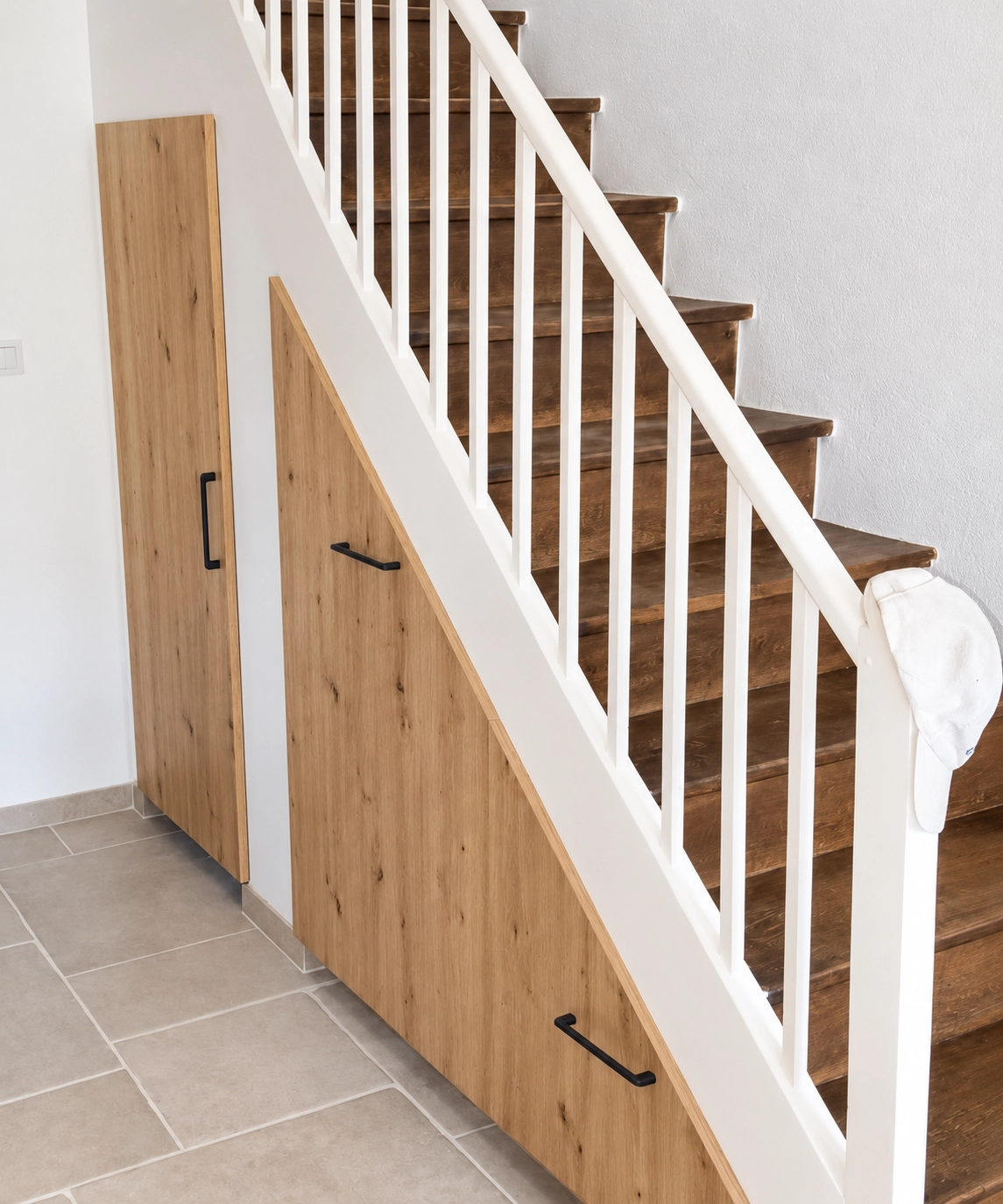 Vue d'ensemble d'un aménagement de rangement sur mesure sous un escalier avec des façades effet bois et des poignées noires.